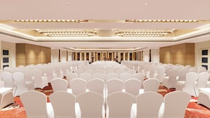 A large conference room with rows of white chairs, a stage with a podium, and a modern chandelier. - The Aarlis Hotel Panchkula, Vignette Collection by IHG (Panchkula)