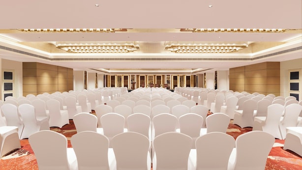 A large conference room with rows of white chairs, a stage with a podium, and a modern chandelier. - The Aarlis Hotel Panchkula, Vignette Collection by IHG (Panchkula)