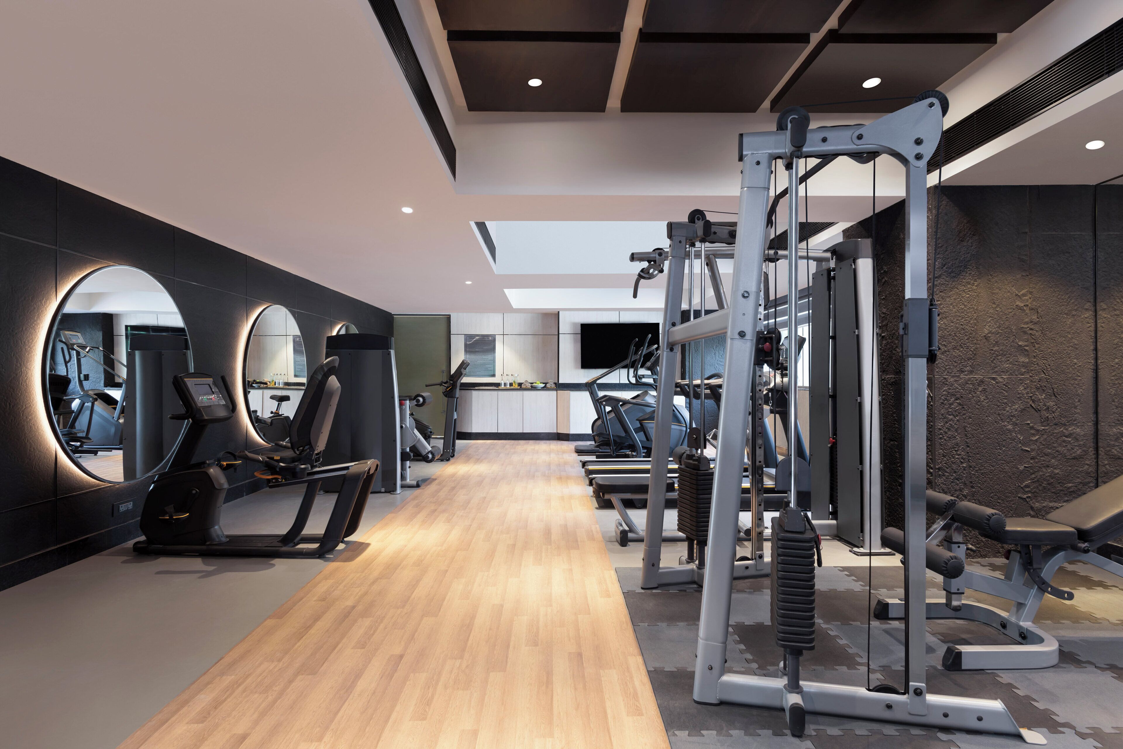 Un gimnasio moderno con equipamiento de ejercicio, piso de madera y un espejo grande.