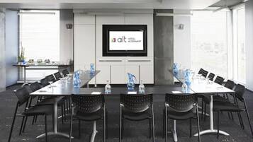 A conference room with a large screen displaying the logo of 'alt hotel alternatf', black chairs, and a long table with water bottles and documents.