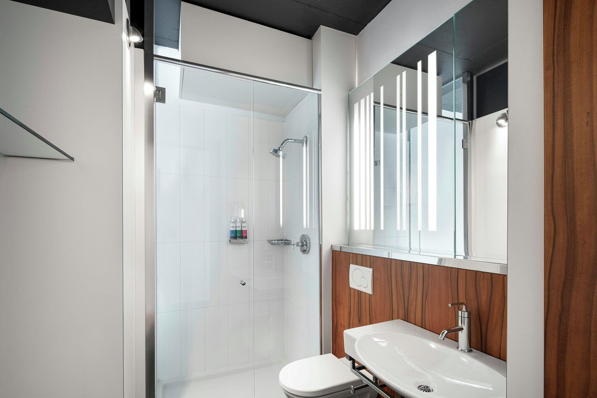 A modern bathroom with a glass-enclosed shower, a wooden vanity, and a large mirror.