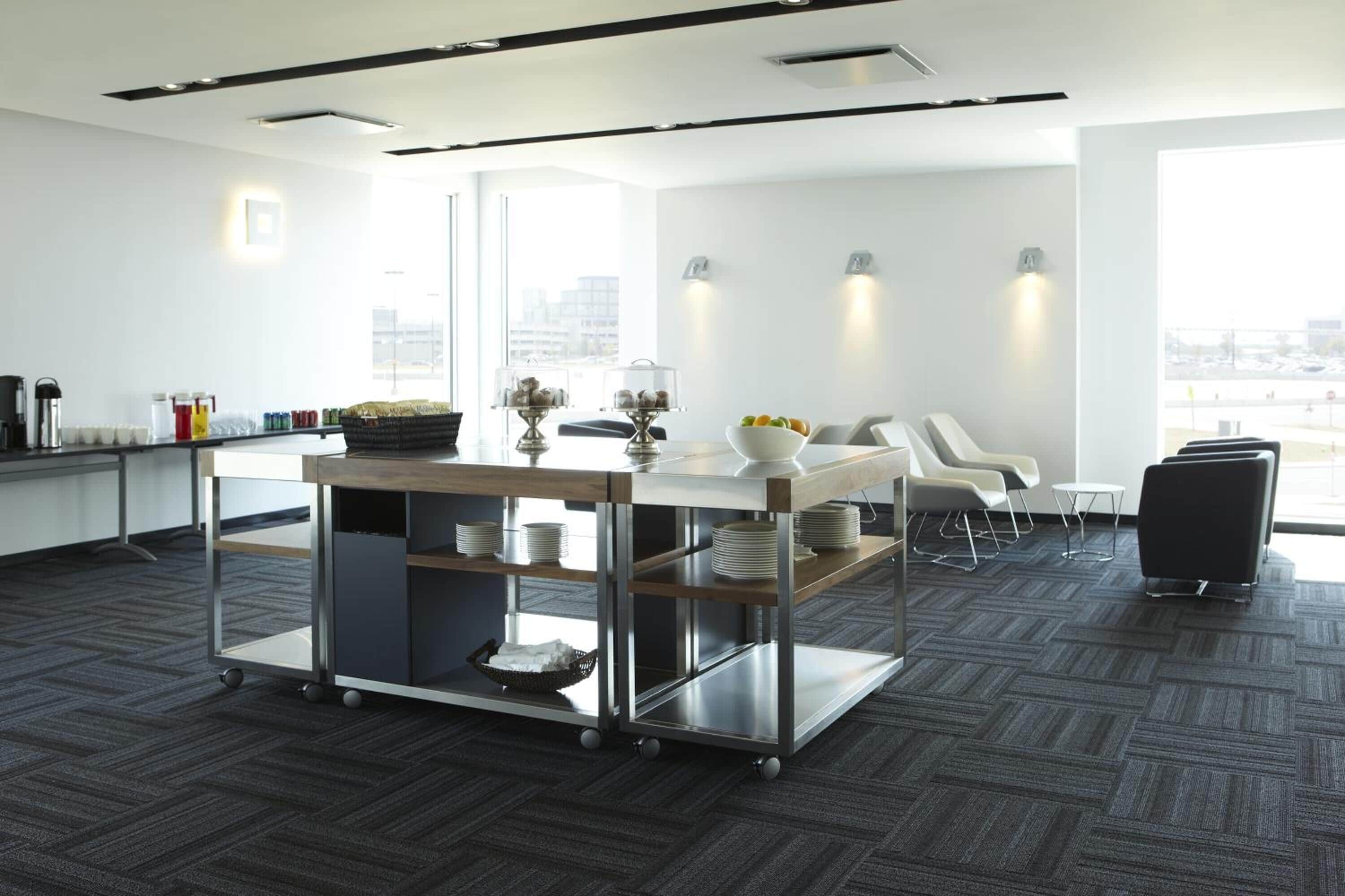 A modern office kitchen with a cart, white chairs, and a view of the city.