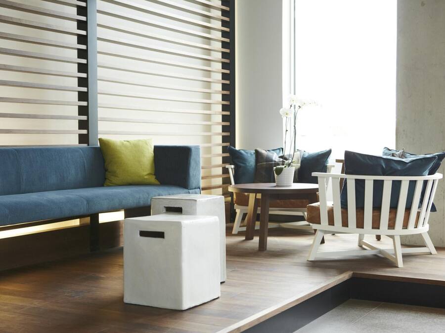 A modern living room with a blue sofa, white ottomans, a wooden coffee table, and a white chair.