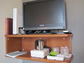 Un televisor sobre una estantería de madera con un mando a distancia, libros, un hervidor y una pequeña bandeja con objetos.