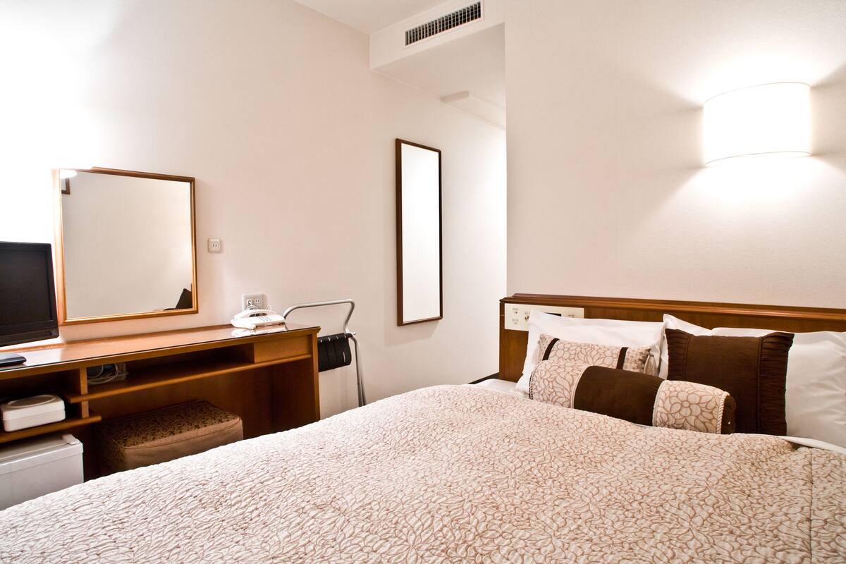 Ein Hotelzimmer mit Bett, Schreibtisch mit Computer, Spiegel und Wandleuchte.