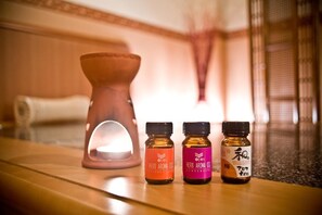 Tres pequeñas botellas de aceite aromático a hierbas sobre una superficie de madera, con una vela al fondo.
