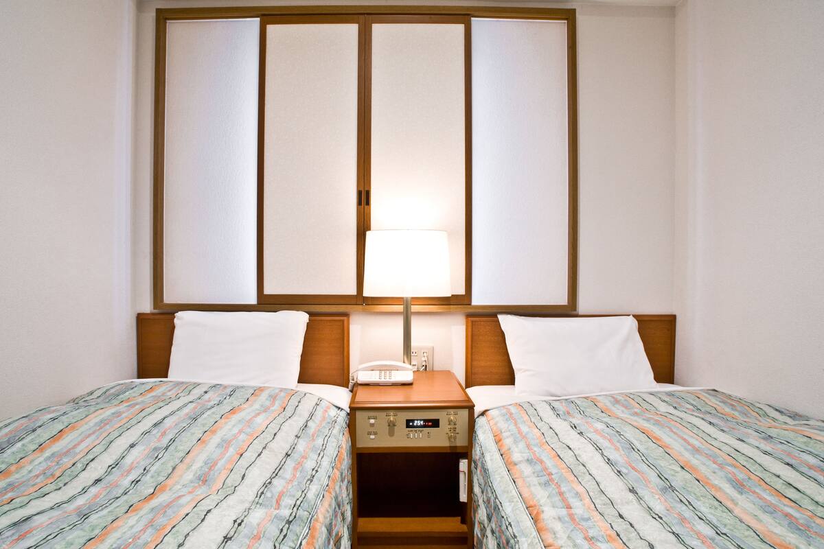 Ein Hotelzimmer mit zwei Betten, einem Nachttisch mit Lampe und einem großen Fenster mit Blick.