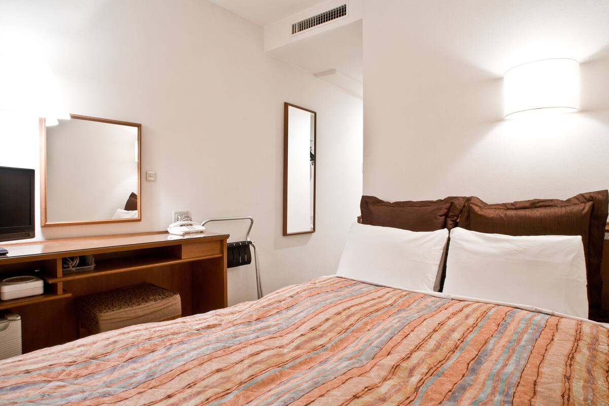 Ein Hotelzimmer mit Bett, Schreibtisch, Fernseher und Spiegel.