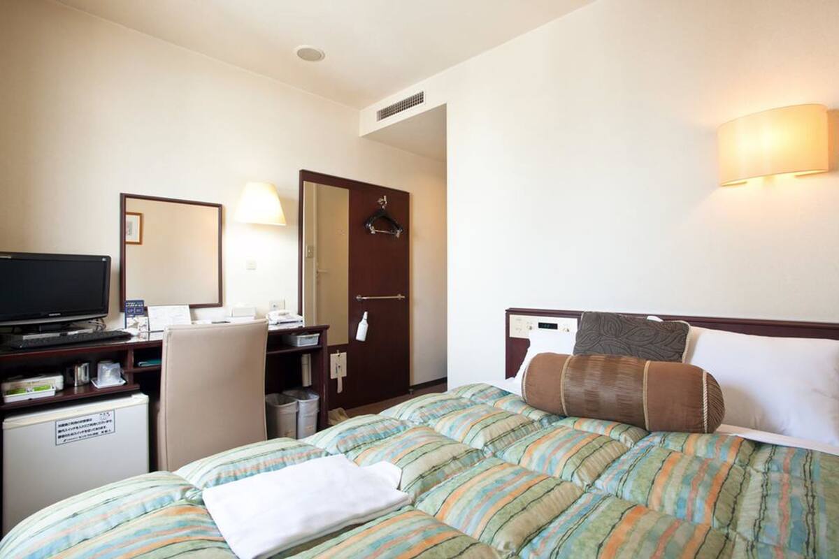 A hotel room with a bed, a desk with a computer, a television, and a small refrigerator.