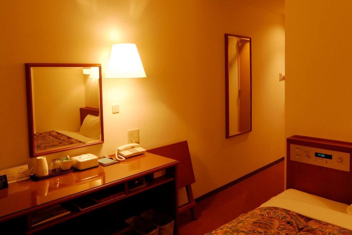 Ein Hotelzimmer mit einem Bett, einem Schreibtisch mit Telefon, einem Spiegel und einer Wanduhr.