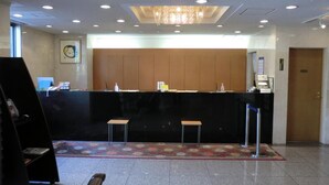 A hotel reception area with a black reception desk, two stools, a chandelier, and a tiled floor. - Kuretake Inn Iwata (Iwata)