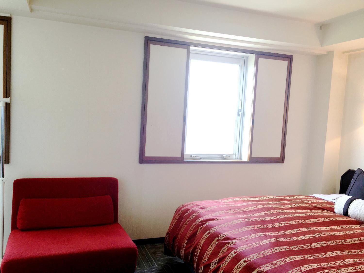 Ein Hotelzimmer mit einem Einzelbett, einem roten Sessel und einem Fenster mit Blick.