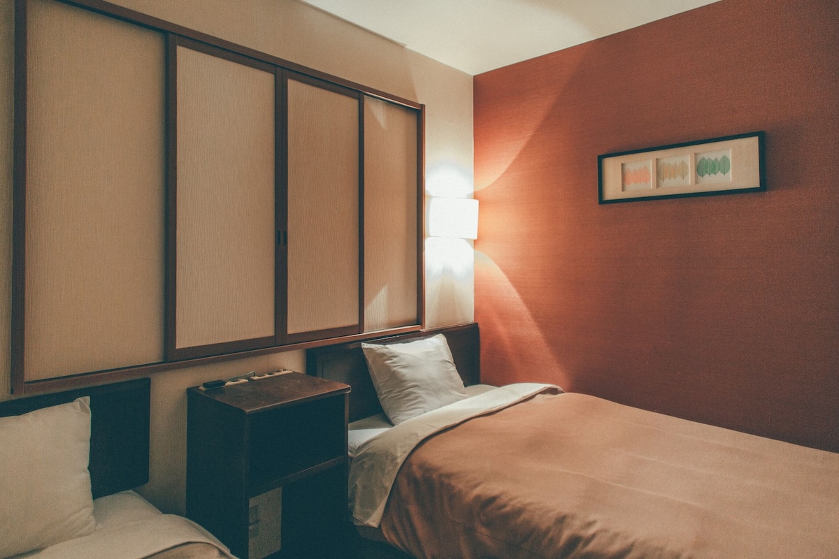 A hotel room with a bed, a nightstand, a wall-mounted panel, and a framed picture.
