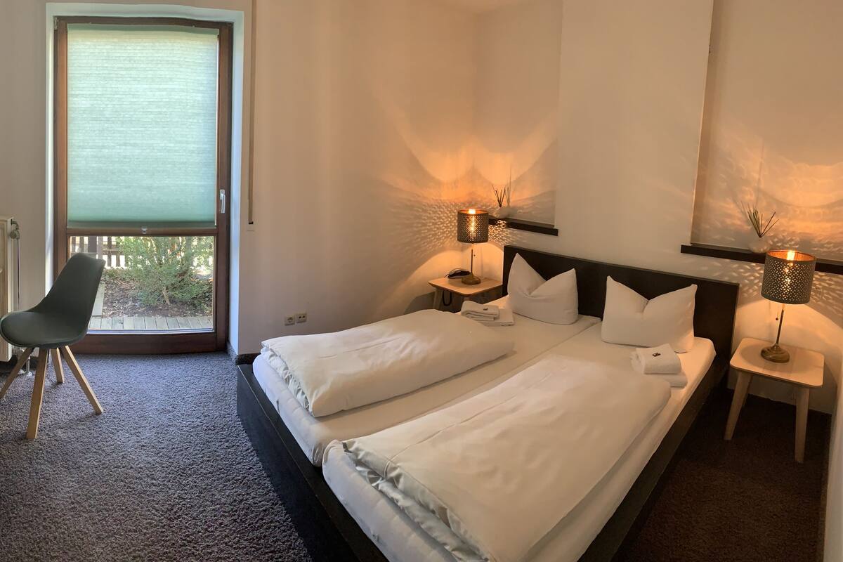 A hotel room with a bed, desk, chair, and two bedside lamps.