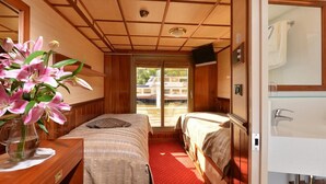 A room with two beds, a wooden ceiling, a large window, and a bathroom with a glass shower.