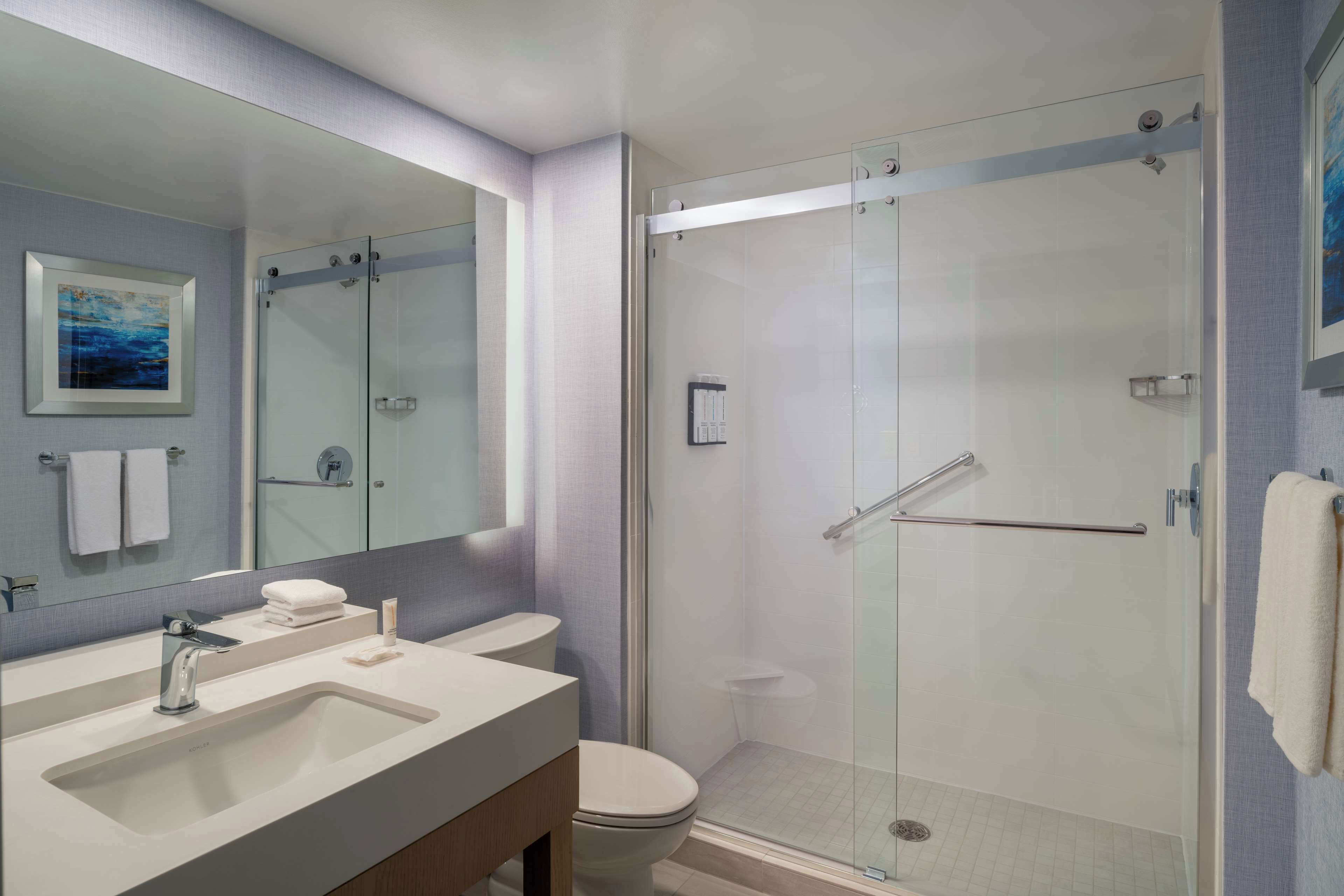 A modern bathroom with a glass-enclosed shower, a large mirror, and a sink with a vanity.
