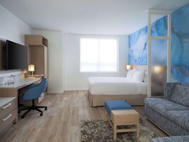 Una habitación de hotel moderna con cama, escritorio con silla, sofá y un ventanal grande.