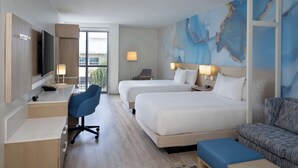 A hotel room with two beds, a desk with a TV, a chair, a sofa, and a large abstract wall mural.