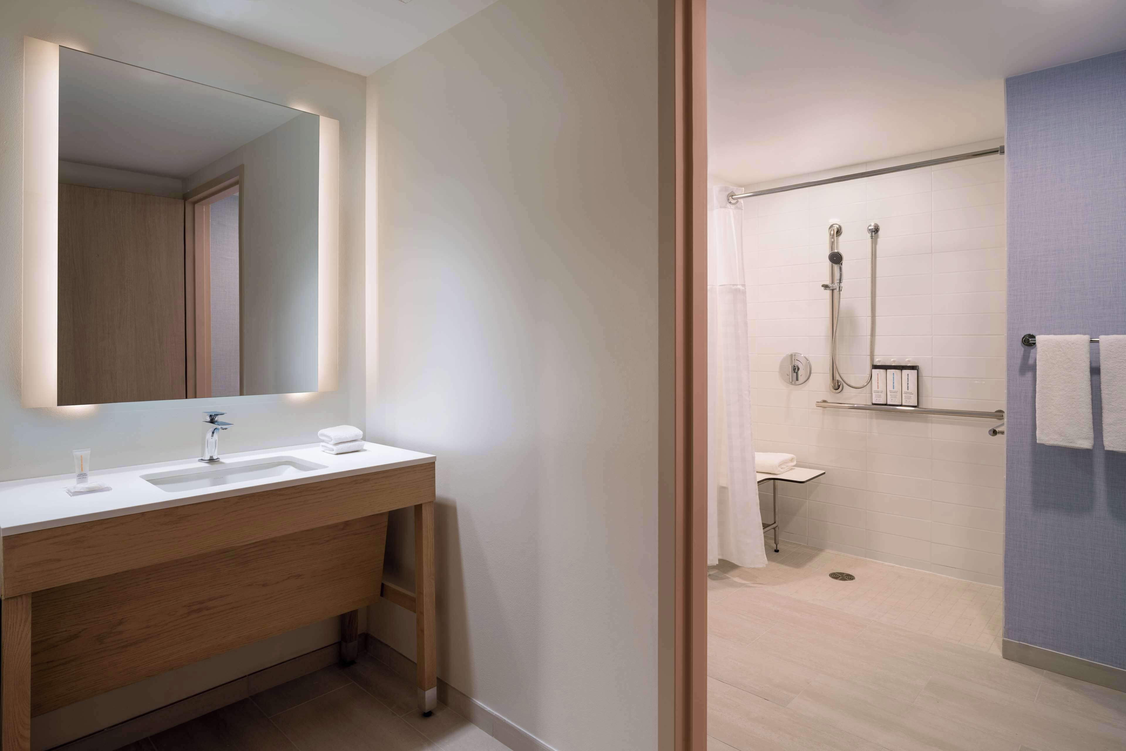 A modern bathroom with a wooden vanity, a large mirror, and a shower area.