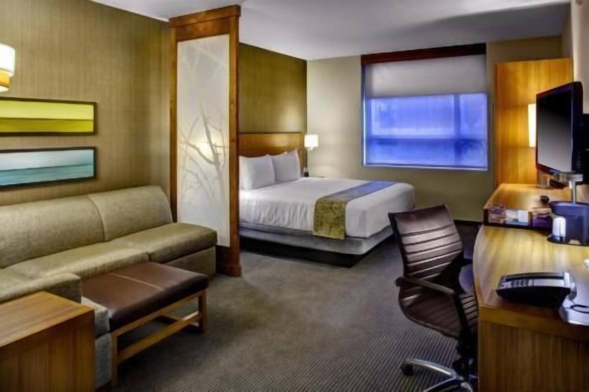 Ett hotellrum med en säng, en soffa, ett skrivbord, en stol och en tv.