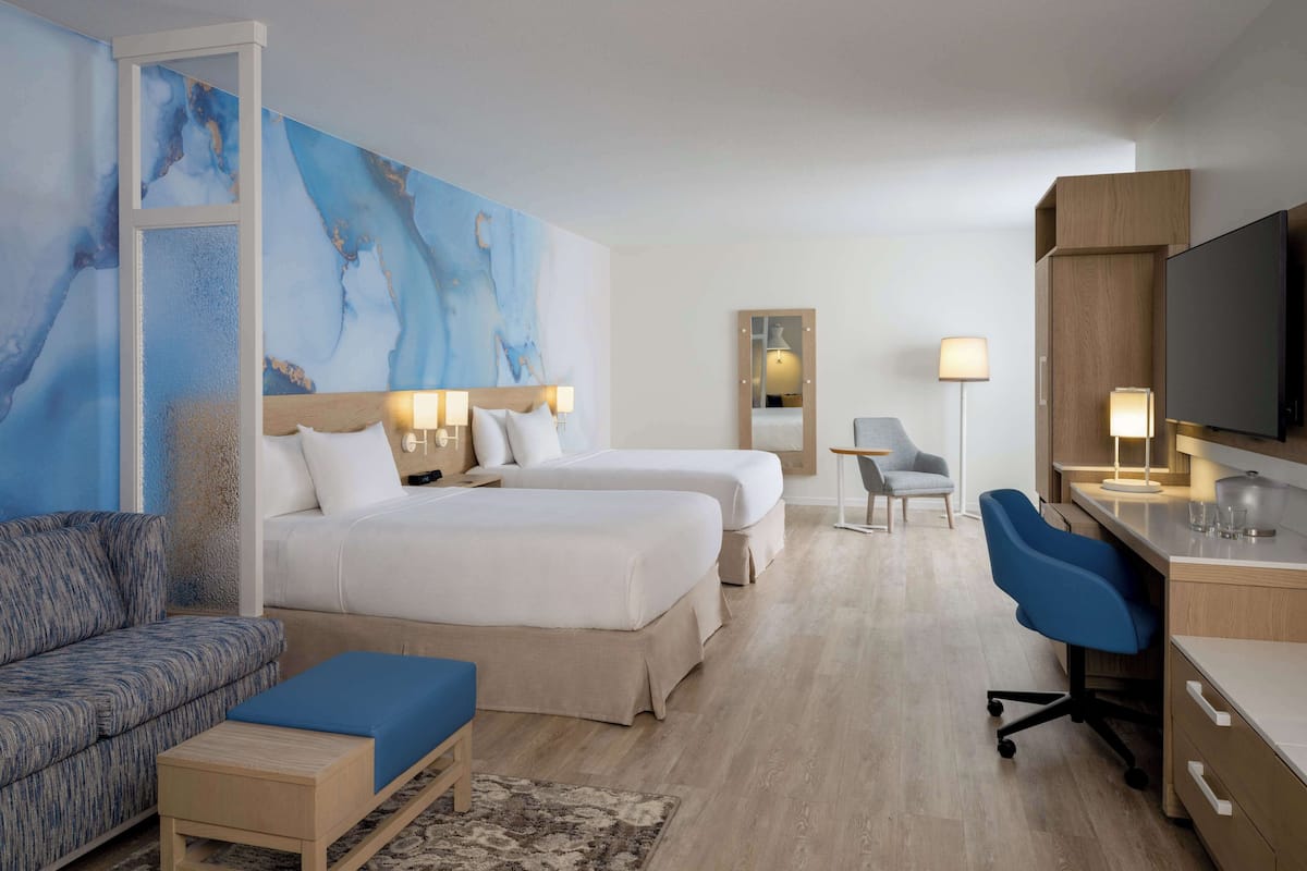 Ett hotellrum med två sängar, ett skrivbord, en tv och en stor, abstrakt målning på väggen.
