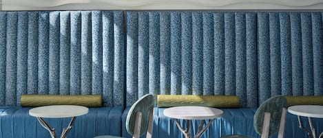 A room with a blue patterned sofa, two chairs with round tables, and a textured ceiling.