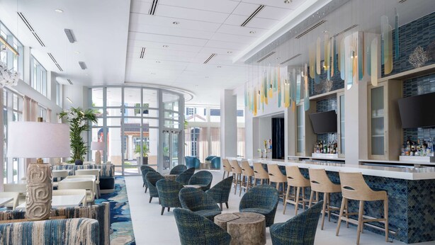 A modern hotel lobby with a bar area, seating arrangements, and large windows.