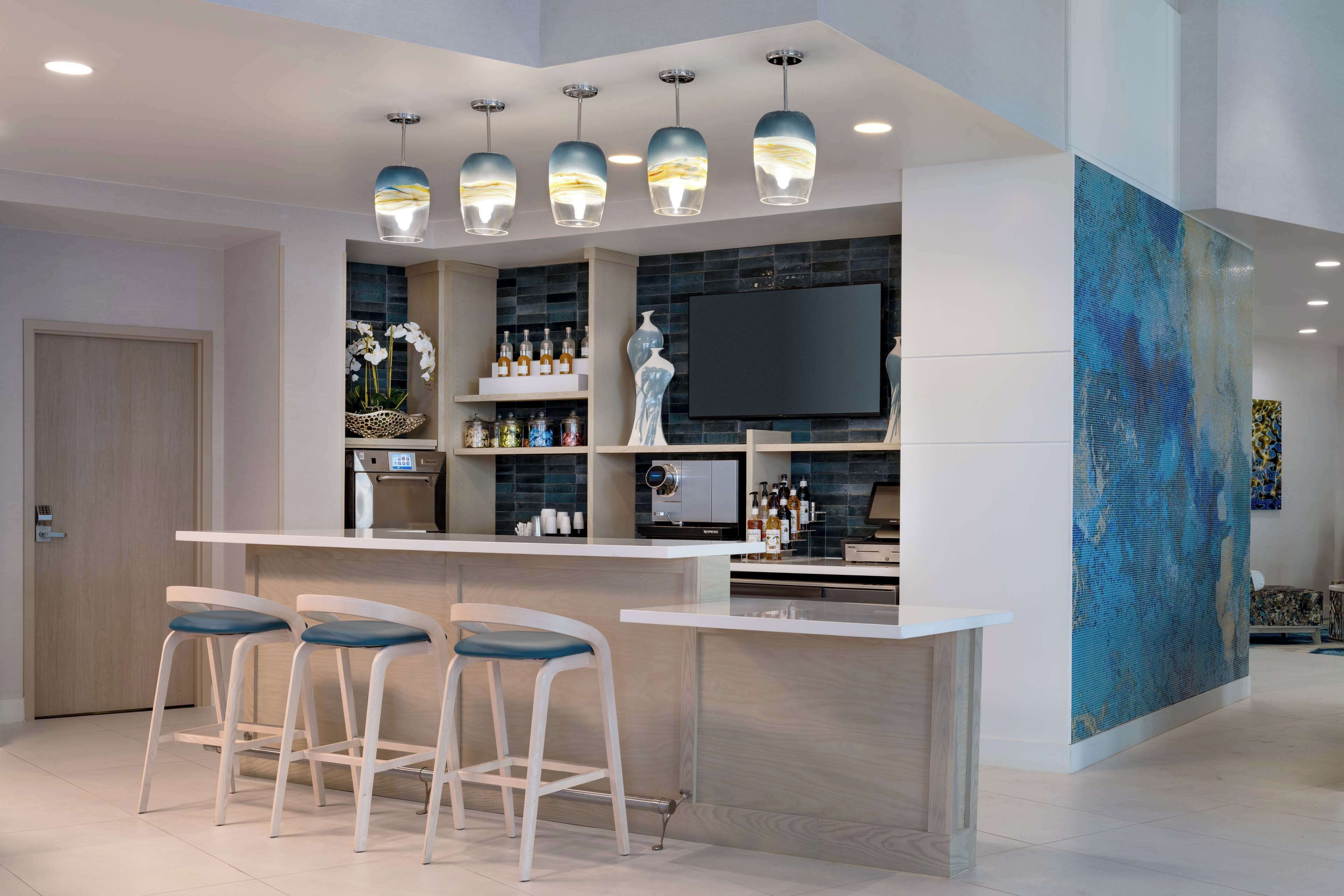 A modern kitchen with a bar area, bar stools, a flat-screen TV, and a large abstract painting.