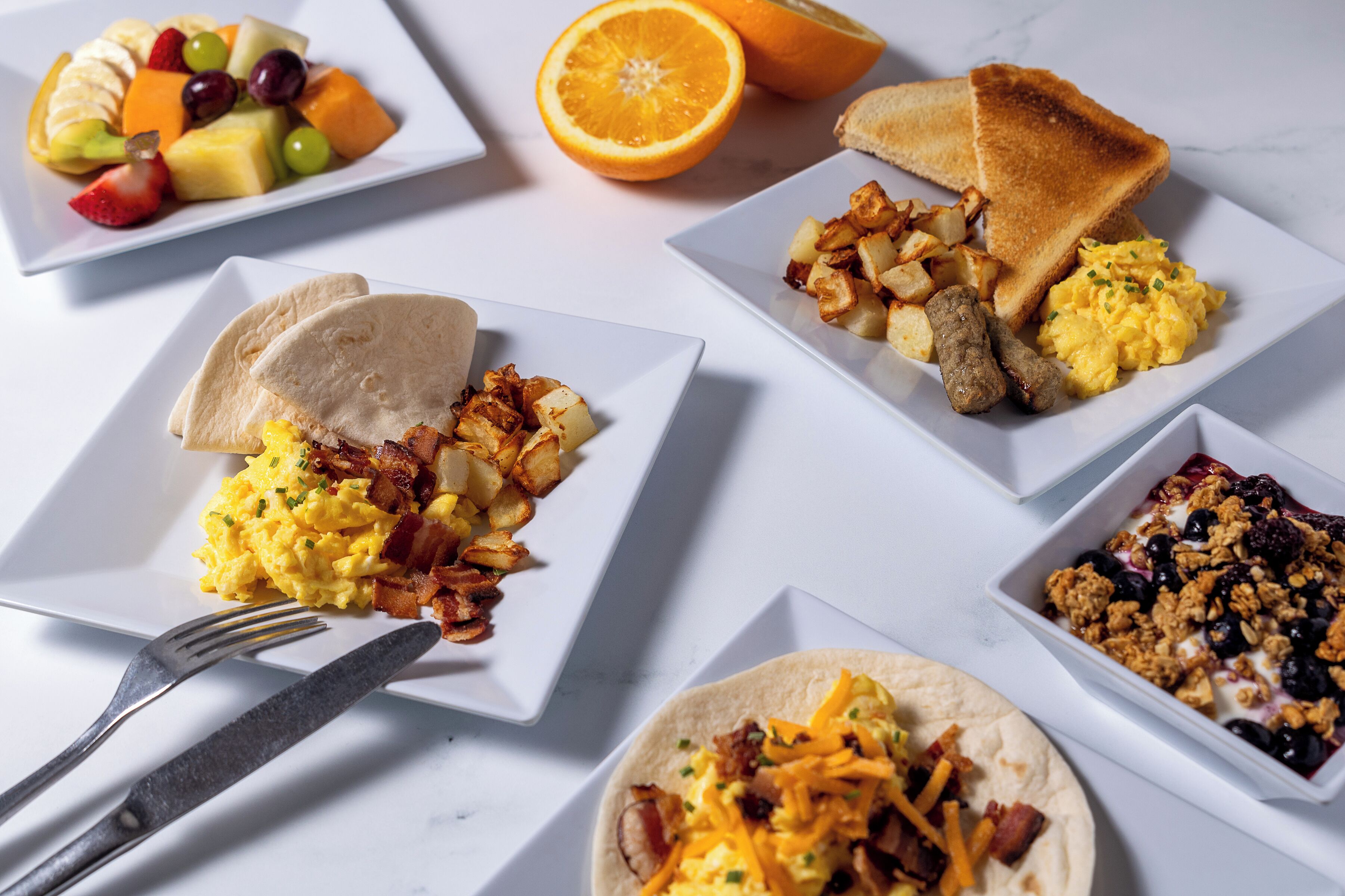 A breakfast spread with various dishes including scrambled eggs, toast, fruit, and a yogurt parfait.