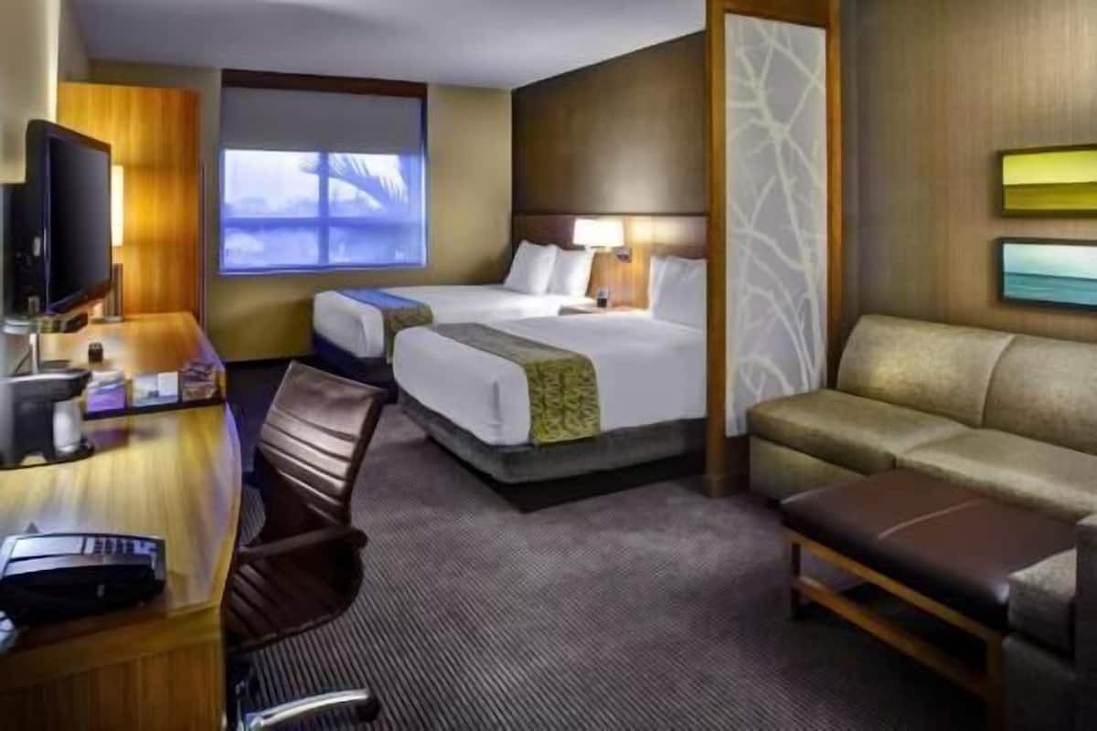 Ett hotellrum med två sängar, en soffa, ett skrivbord med en tv och ett fönster med utsikt.