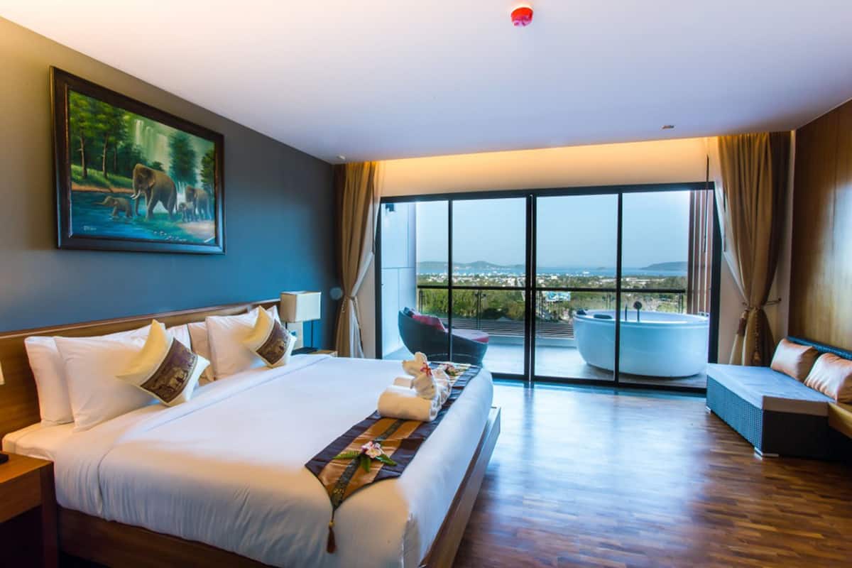 A spacious hotel room with a large bed, a view of a hot tub, and a painting of elephants on the wall.