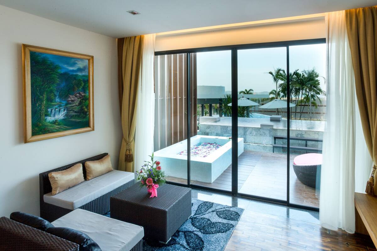 A modern hotel room with a large sliding glass door leading to a pool area, a cozy seating area with a sofa and a coffee table, and a painting on the wall.