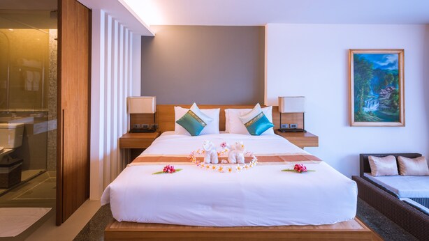 Una habitación de hotel con una cama grande, dos mesitas de noche, un cabecero de madera, un cuadro en la pared y una zona de ducha con mampara de vidrio.