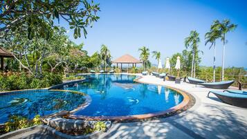 A pool with a curved design, surrounded by lounge chairs and palm trees.
