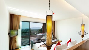 Habitación de hotel moderna con una cama grande, televisión, balcón con vistas y dos lámparas colgantes.