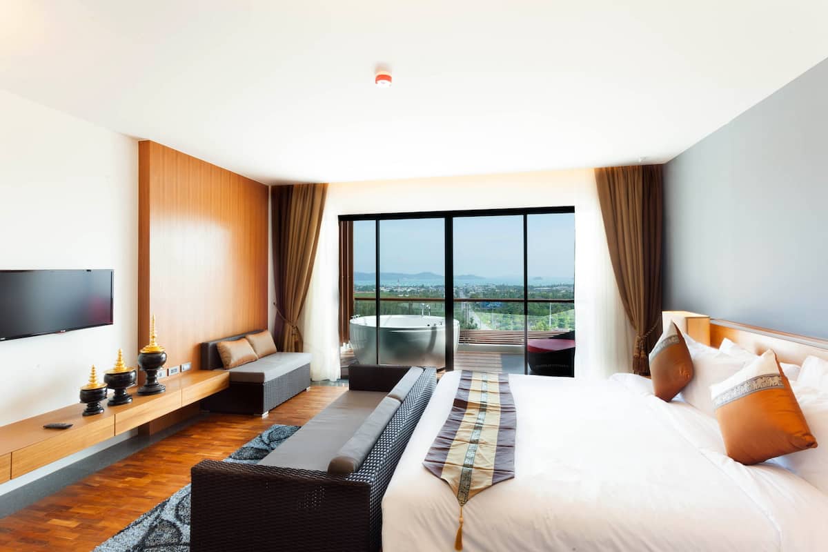 A modern hotel room with a large bed, a flat-screen TV, a seating area, and a balcony with a city view.