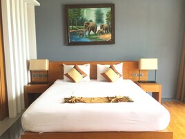 Une chambre d’hôtel avec un grand lit, deux tables de chevet avec des lampes, un tableau représentant des éléphants accroché au mur et un rideau sur le côté gauche.