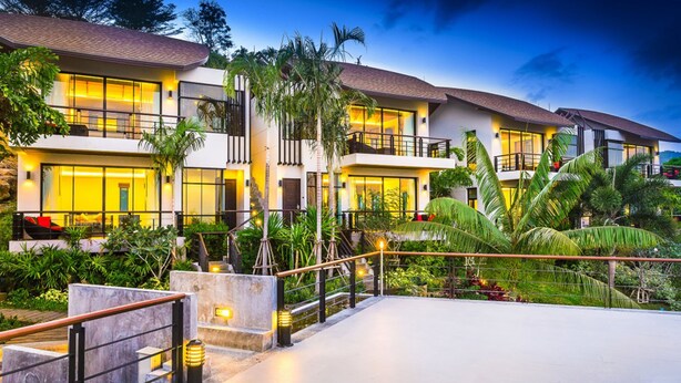 Un hotel de varios pisos con balcones, un jardín ajardinado y un exterior bien iluminado.