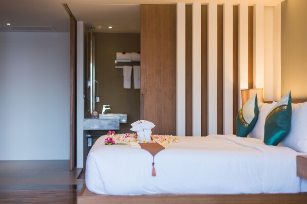 Habitación de hotel con una cama grande, cabecera de madera y baño visible a través de una puerta abierta.