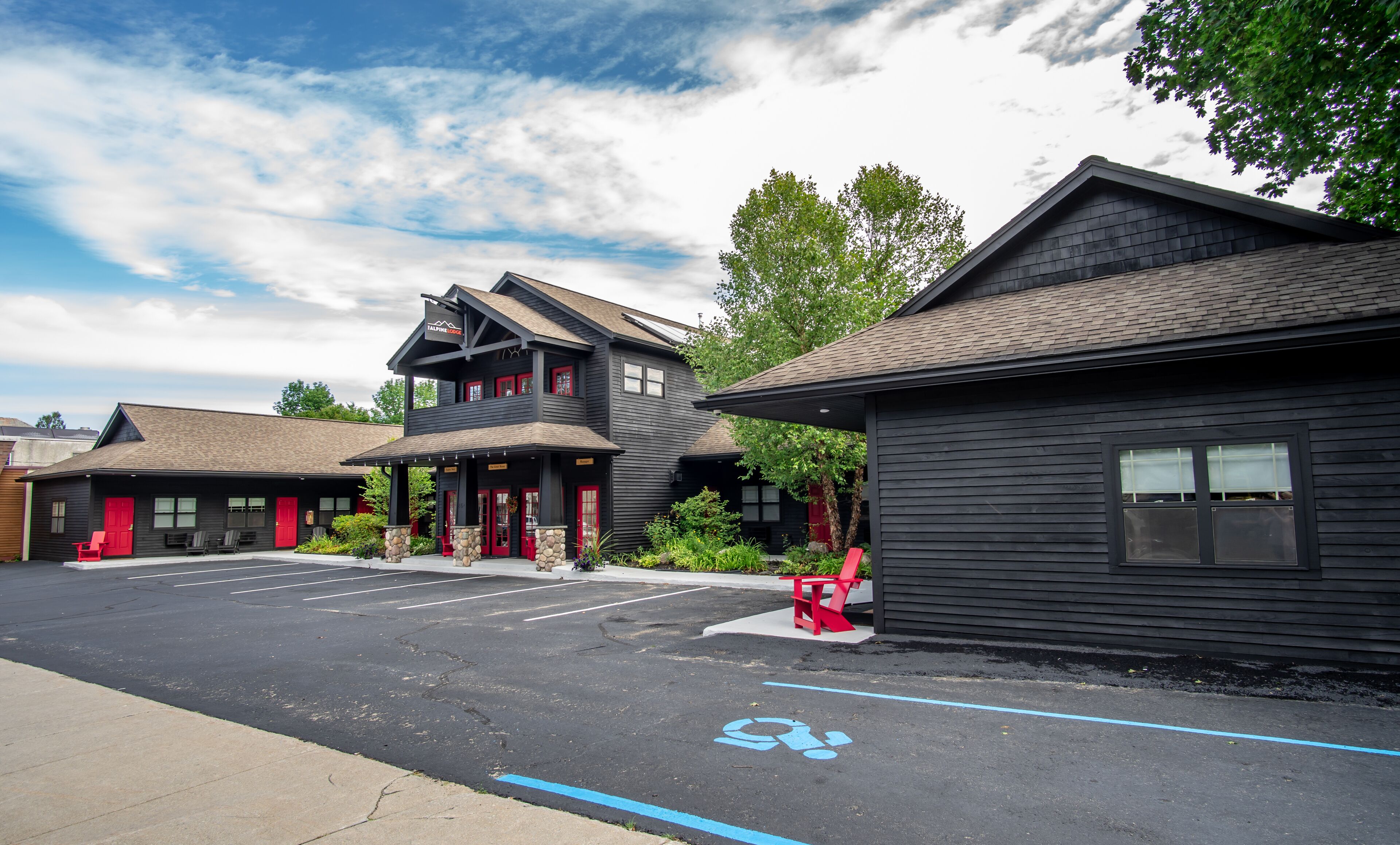 A row of dark wooden buildings with red doors, a parking lot, and a blue handicapped parking sign.