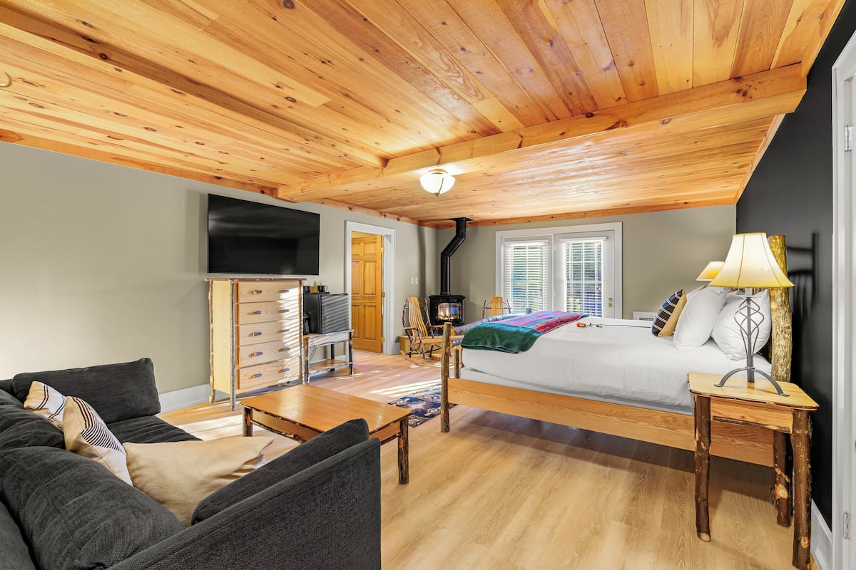 A cozy room with a wooden ceiling, a bed, a TV, a fireplace, and a dining area.