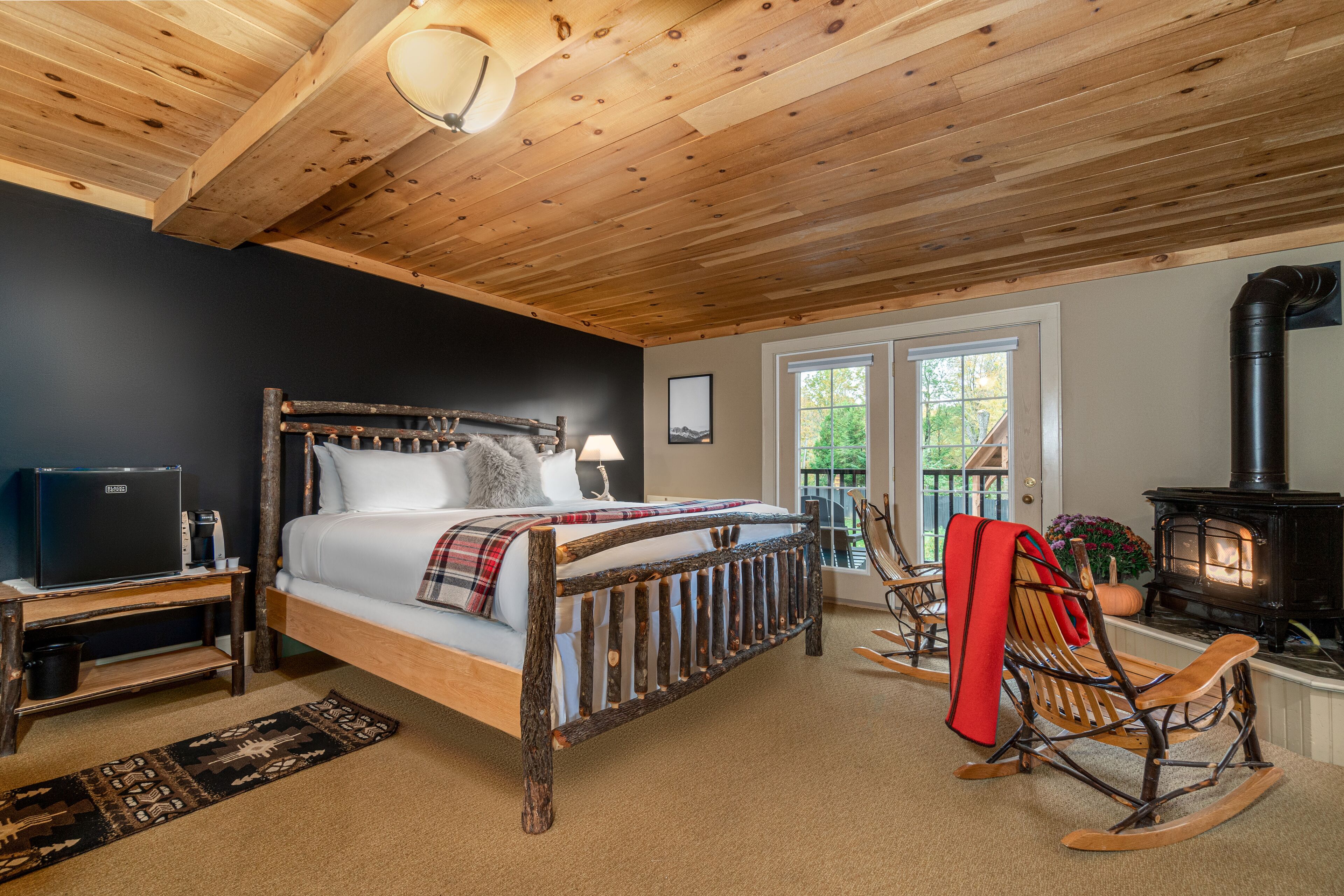 Une chambre confortable avec un lit en bois, un téléviseur posé sur un meuble en bois, un fauteuil à bascule et une cheminée.