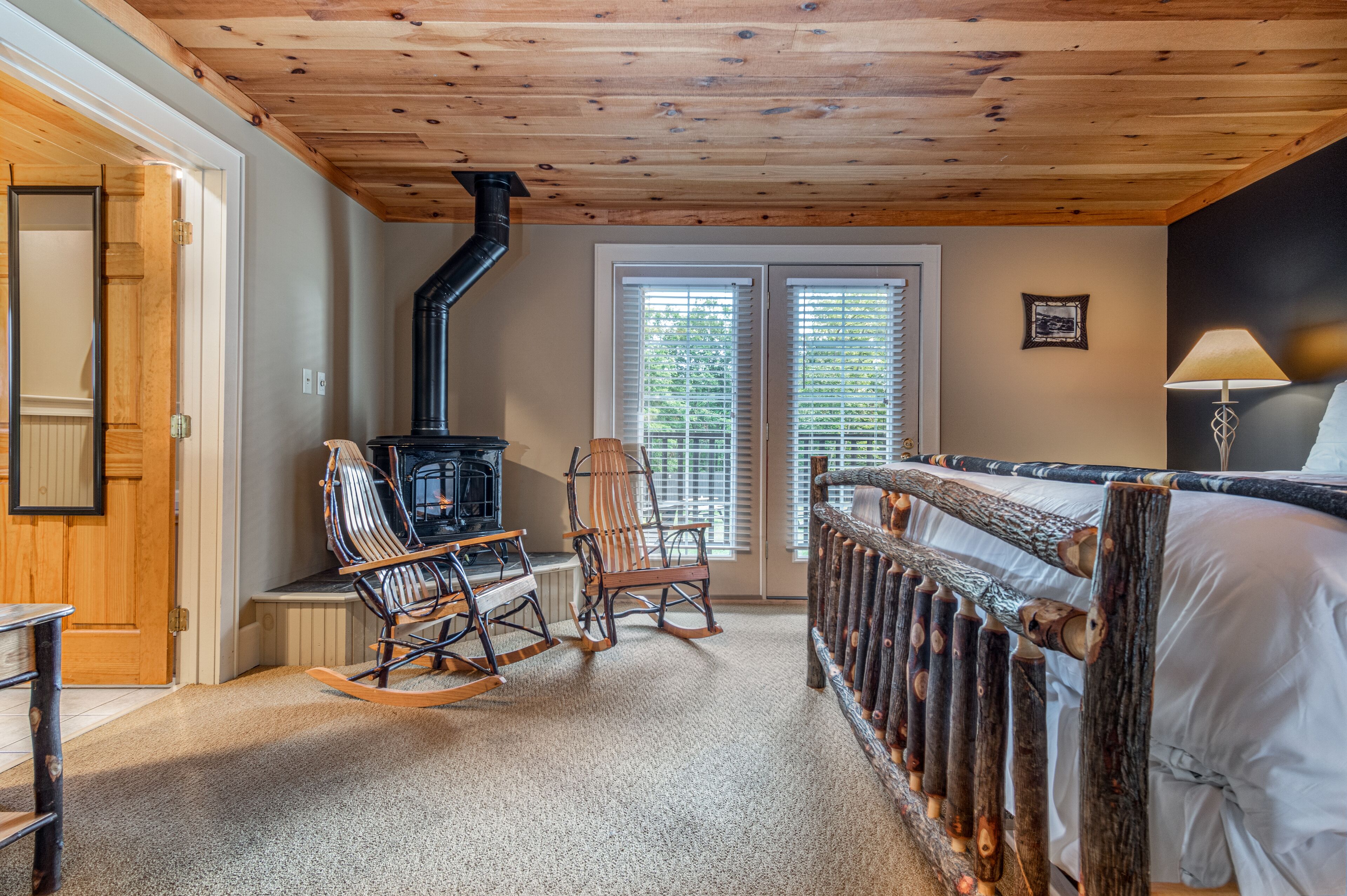 Una habitación acogedora con techo de madera, chimenea, sillones mecedores y una cama con cabecera de madera.