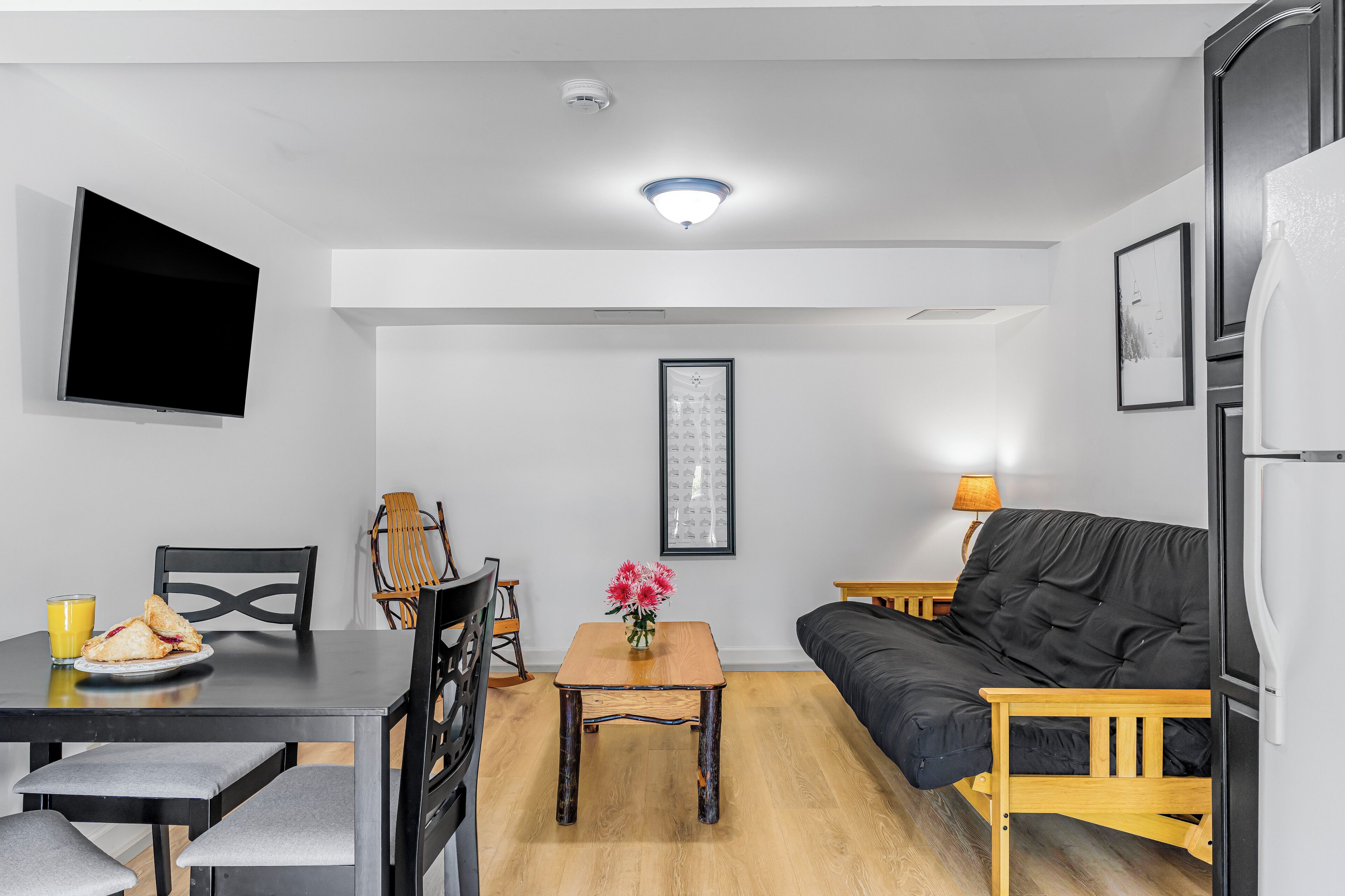 Ein gemütlicher Wohnbereich mit Esstisch, Stühlen, einer Couch, einem Flachbildfernseher und einem kleinen Tisch mit Blumen.
