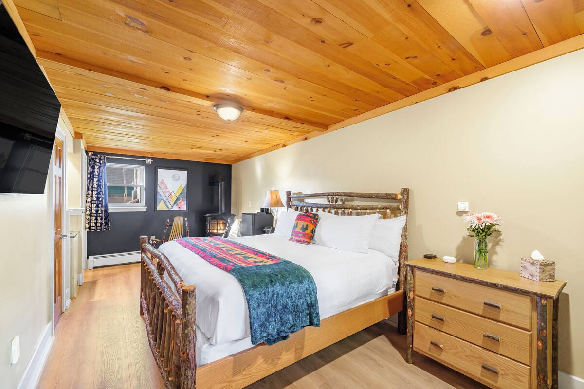 A wooden ceiling, a bed with a colorful blanket, a nightstand, and a dresser.