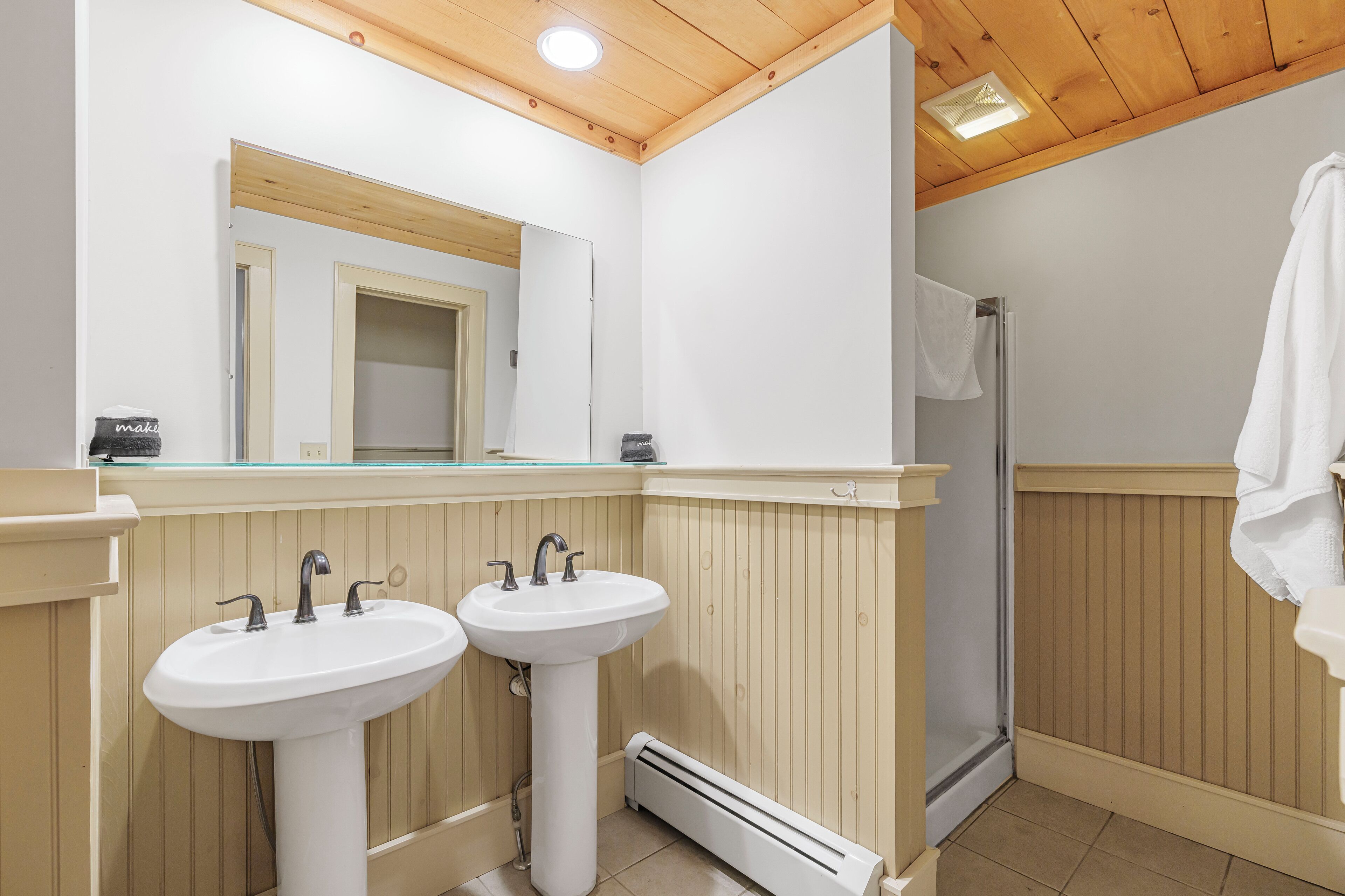 Un baño con dos lavamanos, un espejo, una ducha y paneles de madera.