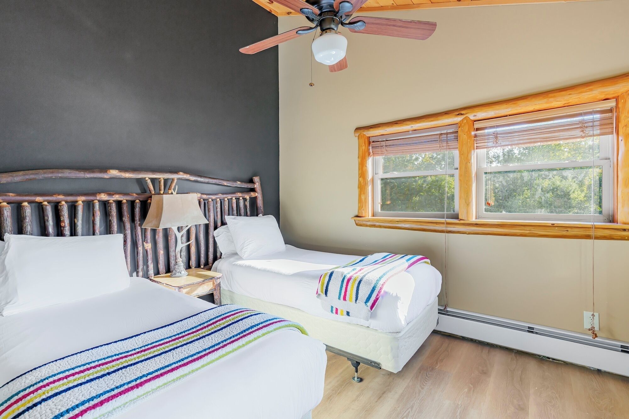 A room with two beds, a wooden headboard, a ceiling fan, and a window with blinds.
