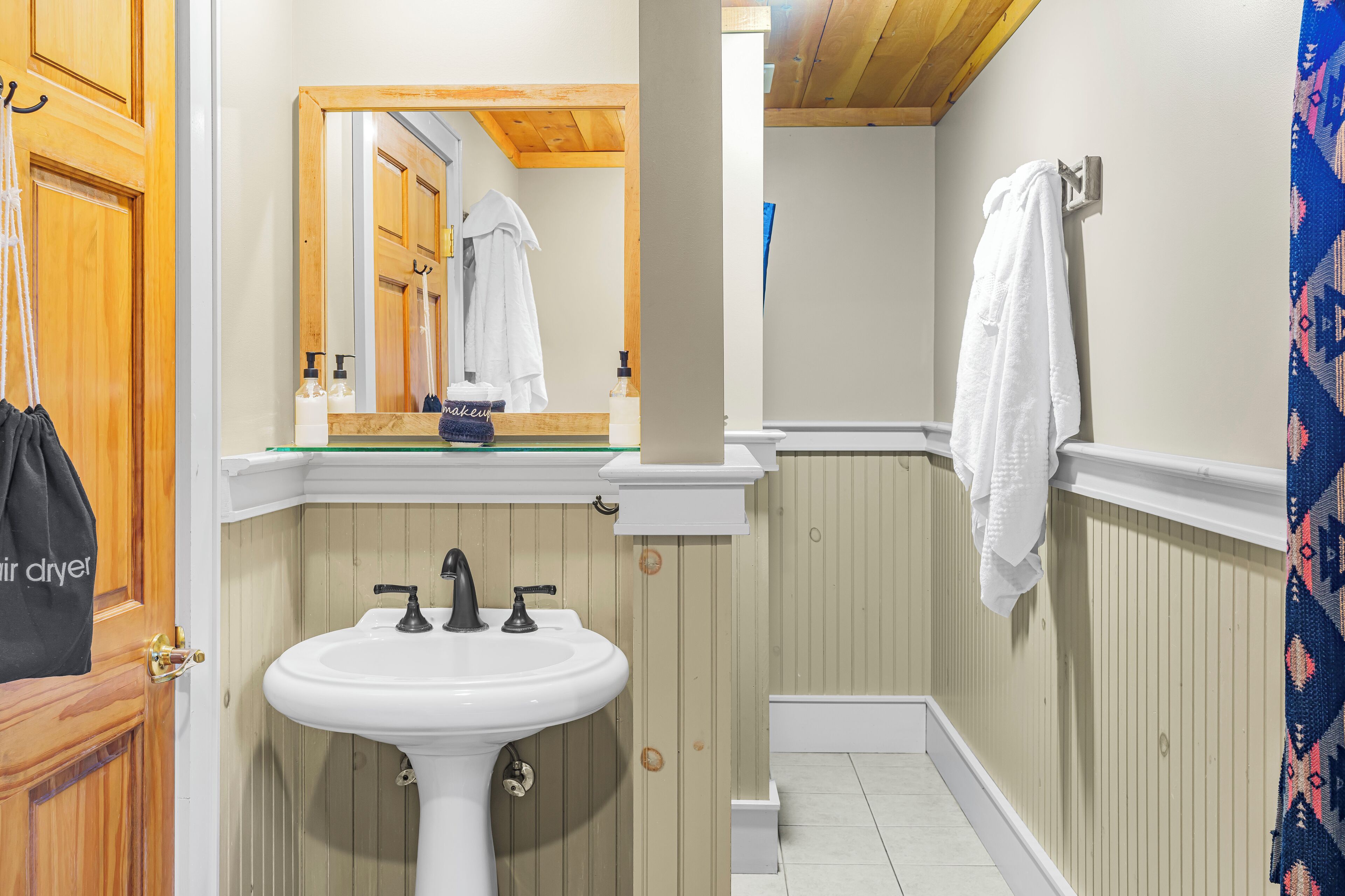 A bathroom with a white sink, wooden paneling, a mirror, and a towel hanging on the wall.