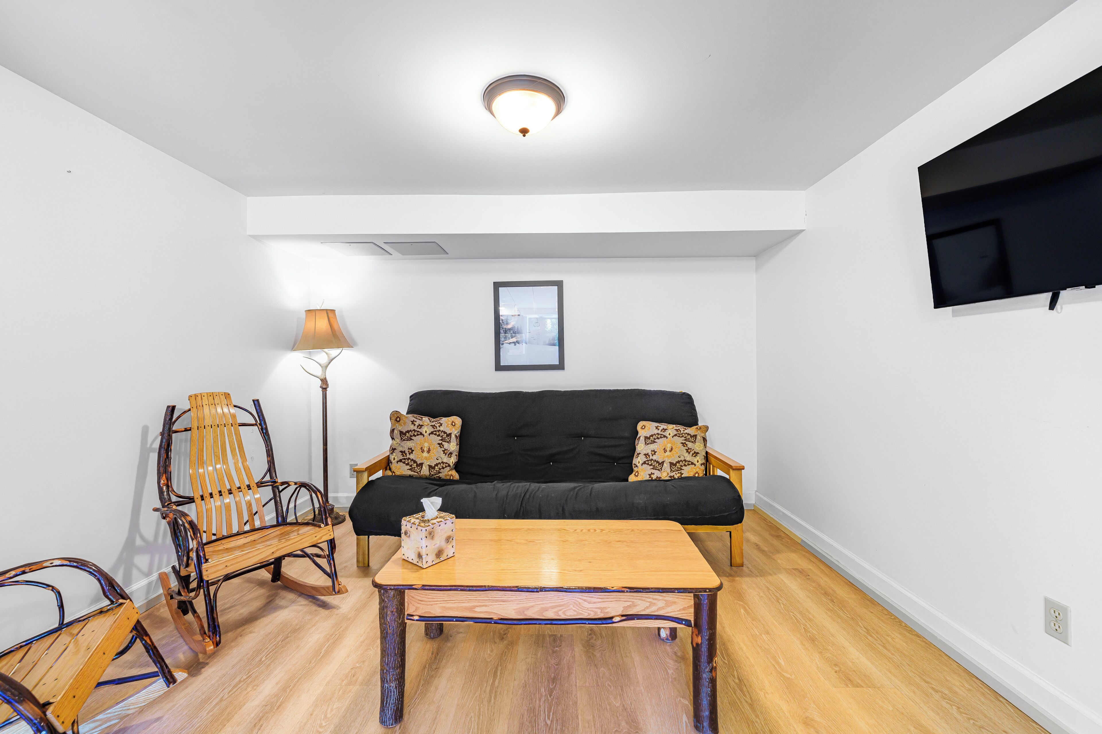 A living room with a black sofa, two patterned pillows, a wooden coffee table, a wooden rocking chair, and a floor lamp.