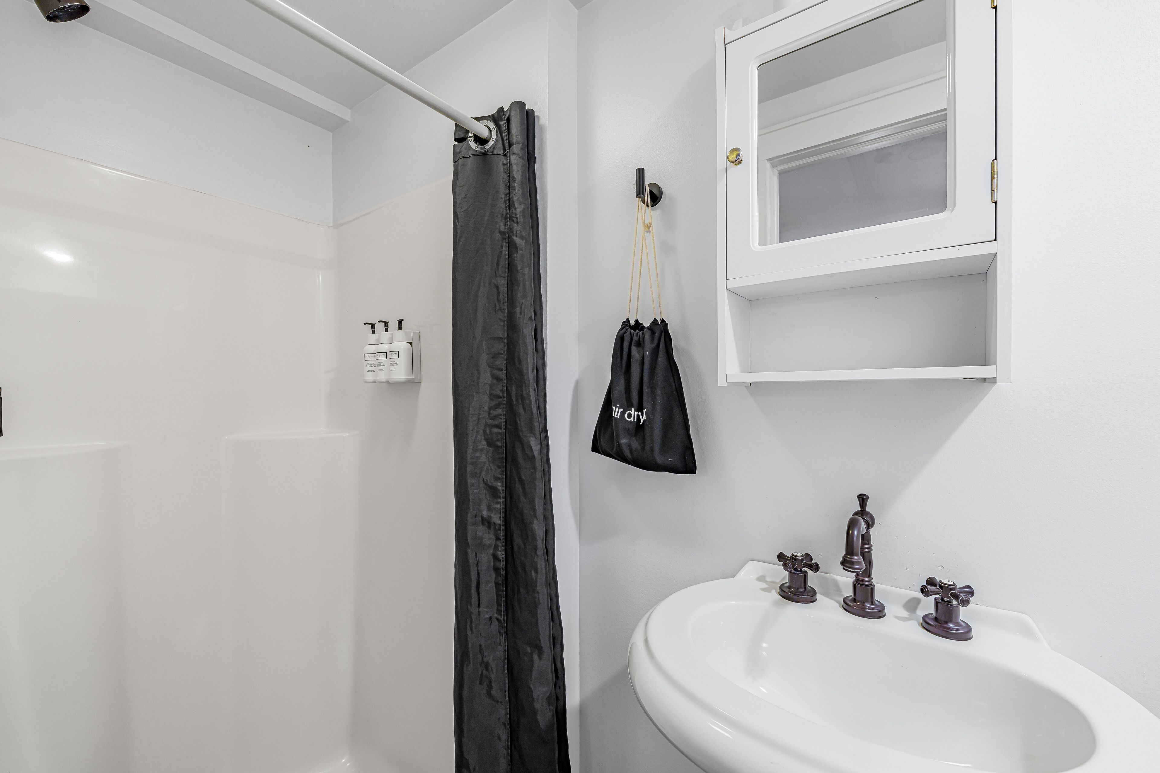 A bathroom with a white sink, three faucets, a mirror, and a shower curtain.